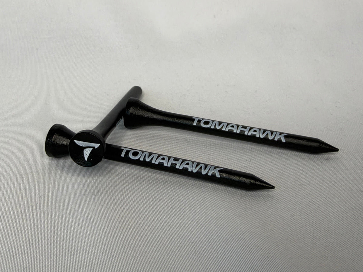 Two black wooden Tomahawk golf tees with white branding, displayed on a light gray background.